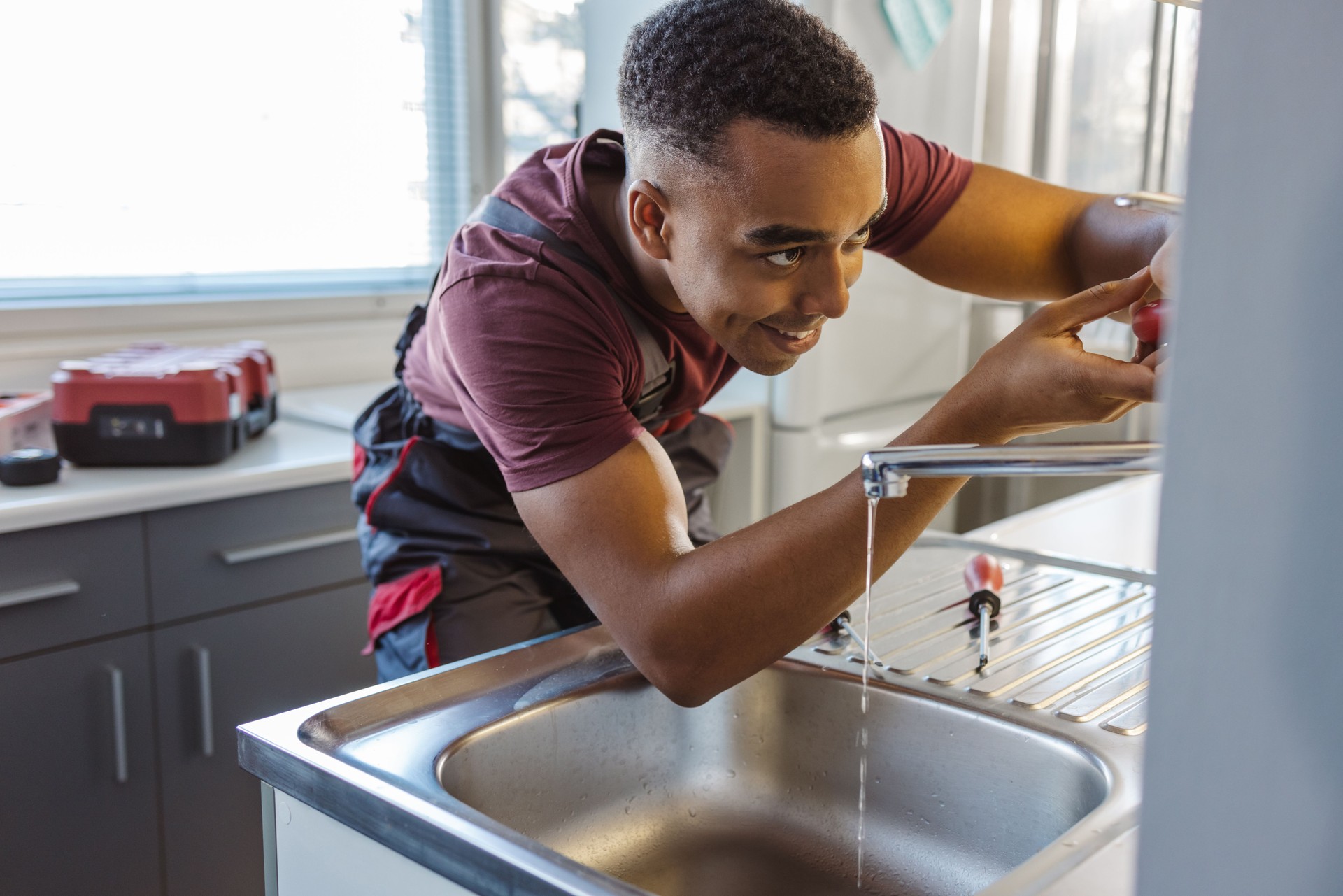 African American male plumber fixing a leak in the kitchen sink at the customer's home