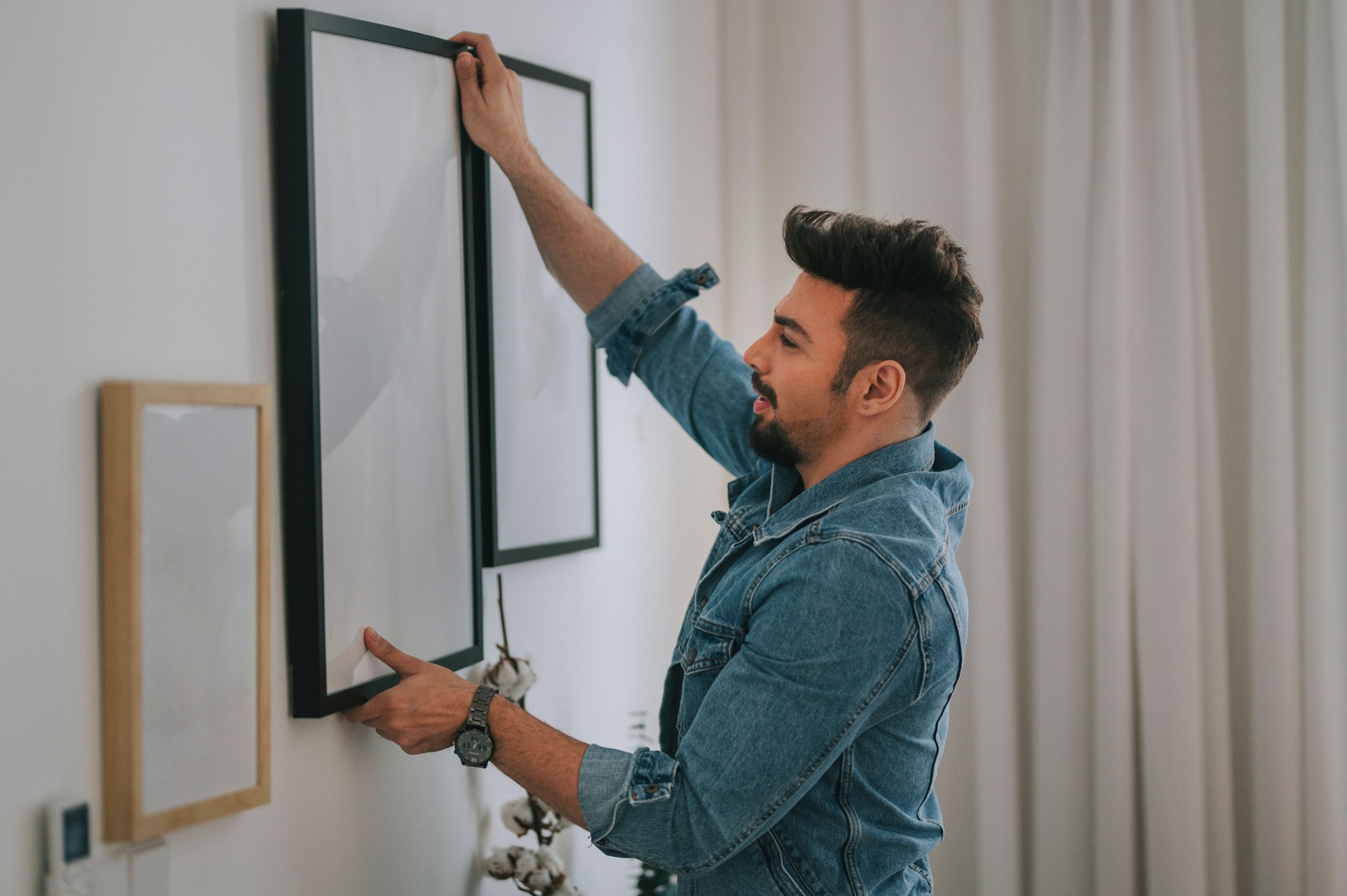 a middle eastern man with beard hanging a painting on the wall at his living room